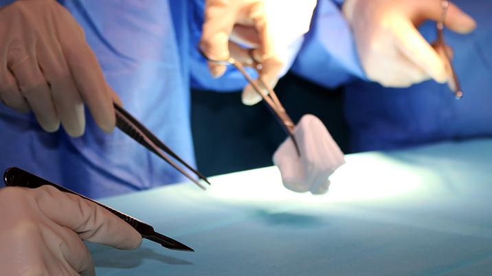 Hands with surgical gloves and equipment around a surgery table