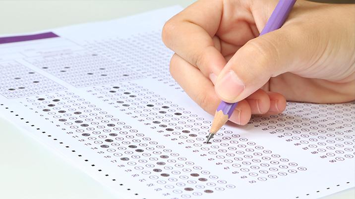 A hand with a pencil filling out an examination paper
